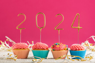 New Years background. Holiday cupcakes with numbers 2022 surrounded by New Years tinsel on pink...