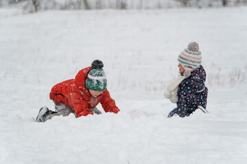Two children are playing in the snow. Children in knitted hats and puffy jackets have fun on winter...