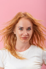 Green-eyed girl on pink background looks to the side. Portrait of young smiling round-faced woman with ginger hair