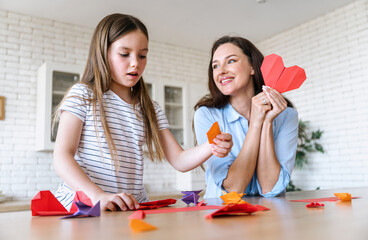 Mother and daughter making origami heart and birds together