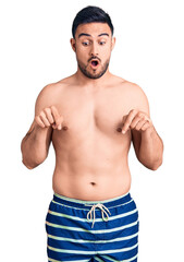 Fototapeta premium Young handsome man wearing swimwear pointing down with fingers showing advertisement, surprised face and open mouth
