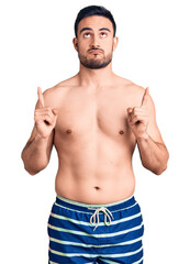 Fototapeta premium Young handsome man wearing swimwear pointing up looking sad and upset, indicating direction with fingers, unhappy and depressed.