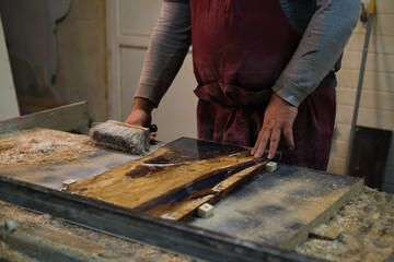 A woodworker applies finish to a beautifully grained slab of wood, revealing the intricate patterns...