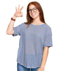Young read head woman wearing casual clothes and glasses smiling positive doing ok sign with hand...