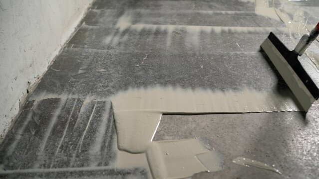 The process of priming a floor with a solution. Waterproofing concrete floor. Industrial primer. The process of priming the floor with a liquid solution using a spatula.