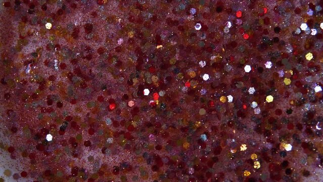 Multicolored particles like confetti or spangles float in a viscous liquid and glitter in the light with depth of field. Glitter texture. Particles background. Shining sparkles.