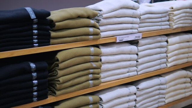 Stack T-shirts different colors and sizes on shelf in department store. Buyers presented assortment T-shirts made from natural fabrics. Quality and nice prices T-shirts will attract attention in store