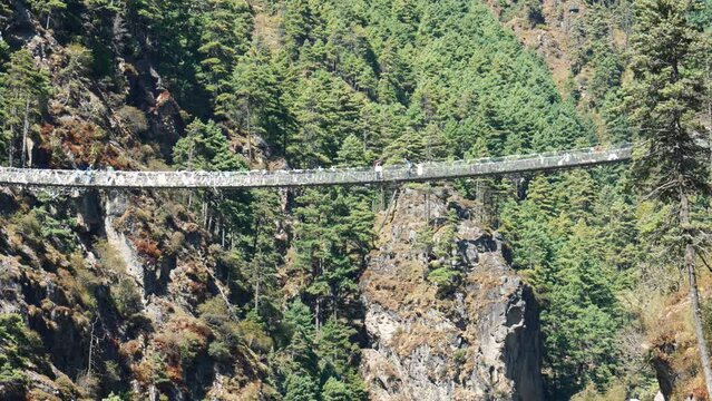 Trekking to Everest Base Camp. Tourists and sherpas with backpacks walk on Hillary suspension bridge through deep rock canyon of Himalayan mountains in Nepal.