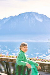 Fototapeta na wymiar Portrait of middle age woman enjoying nice day outside, relaxing on bench in front of mountain lake