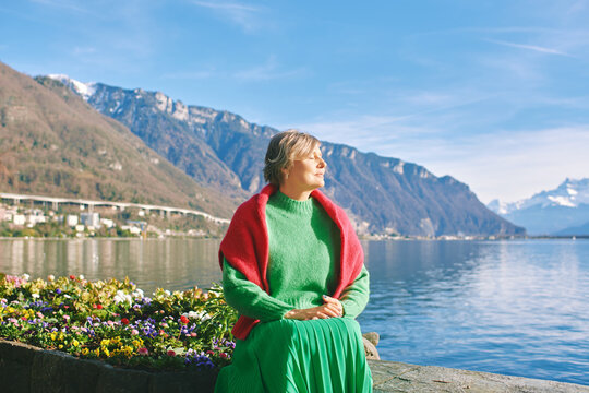 Outdoor portrait of beautiful mature woman posing next to lake, wearing green pullover, healthy lifestyle, image taken in Montrexu, Switzerland