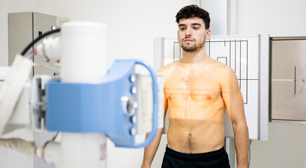 A young Caucasian man undergoes a chest x-ray test inside a hospital to detect cancer, infection or...