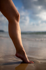 Beautiful female leg on the beach. Sand beach. Sunny evening. Warm sea.