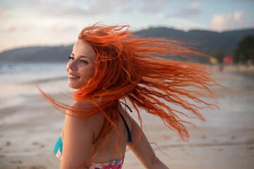 Beautiful girl with red hair posing on the beach. Sunset. Girl with red hair.