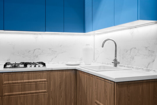 Interior of modern kitchen in blue fnd natural wood tone with cooking stove, sink with beautiful faucet, kitchen concept background