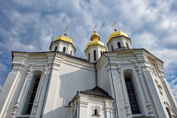 This captivating image captures the grandeur of Catherine's Church in Chernihiv, a pristine white church crowned with resplendent golden domes, harmonizing beautifully with the serene blue sky.