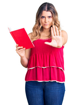 Young caucasian woman holding book with open hand doing stop sign with serious and confident expression, defense gesture