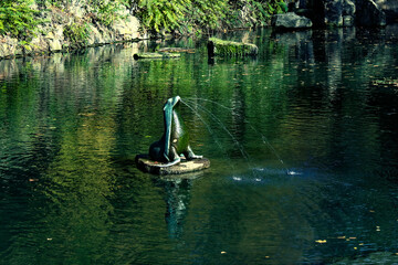 Fototapeta na wymiar A statue is the focal point of this image, with water spraying from its mouth into a pond. Gushing seal sculpture on a park pond.