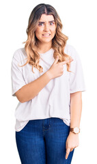 Young caucasian woman wearing casual clothes pointing aside worried and nervous with forefinger,...