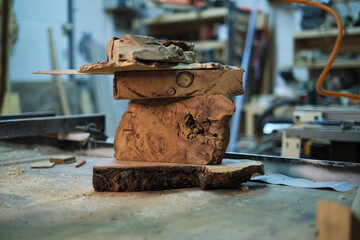 A captivating sculpture of wood burls piled atop one another awaits the creative touch of a woodworker in the midst of a sawdust-filled workshop.