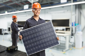 Worker in a uniform holding a solar panel in a factory