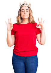 Fototapeta na wymiar Young caucasian woman wearing princess crown relax and smiling with eyes closed doing meditation gesture with fingers. yoga concept.