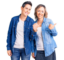 Couple of women wearing casual clothes pointing to the back behind with hand and thumbs up, smiling...