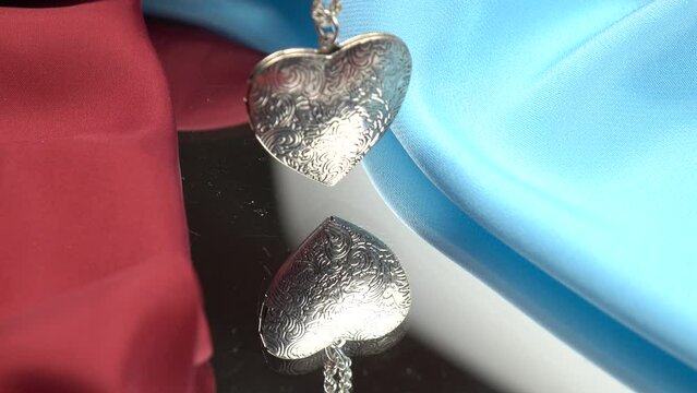 A heart-shaped silver pendant swings on a silver chain, reflected in the mirror