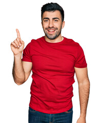 Fototapeta premium Hispanic man with beard wearing casual red t shirt showing and pointing up with finger number one while smiling confident and happy.