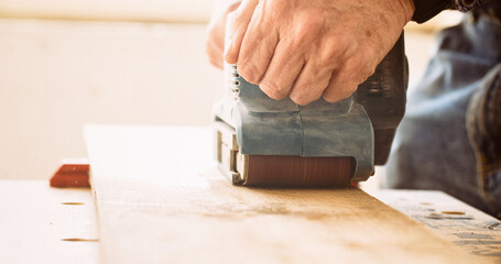 Man sanding wood with a belt sander. DIY and woodwork concept. Shallow focus.