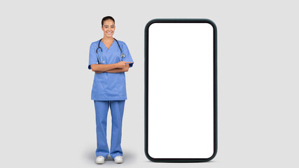 Smiling european young lady doctor or nurse in blue uniform, point finger at big smartphone