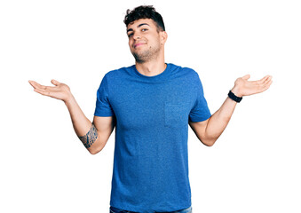 Young hispanic man wearing casual t shirt clueless and confused expression with arms and hands...