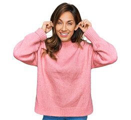 Young hispanic woman wearing casual clothes smiling pulling ears with fingers, funny gesture....