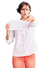 Beautiful young woman with short hair holding blank empty banner pointing with finger to the camera and to you, confident gesture looking serious