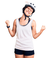 Beautiful young woman with short hair wearing bike helmet very happy and excited doing winner gesture with arms raised, smiling and screaming for success. celebration concept.