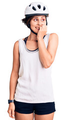 Beautiful young woman with short hair wearing bike helmet looking stressed and nervous with hands on mouth biting nails. anxiety problem.