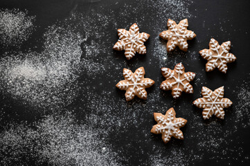 Snowflake sugar gingerbread cookie with frosting decoration, on black table background with flour, flat lay, copy space