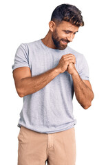 Young hispanic man wearing casual clothes laughing nervous and excited with hands on chin looking...