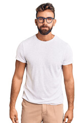 Young hispanic man wearing casual clothes and glasses puffing cheeks with funny face. mouth inflated with air, crazy expression. - obrazy, fototapety, plakaty