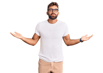 Young hispanic man wearing casual clothes and glasses clueless and confused expression with arms...