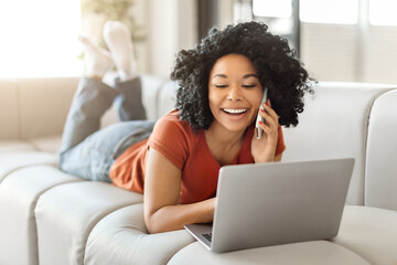 Beautiful Black Woman Using Laptop And Talking On Mobile Phone At Home