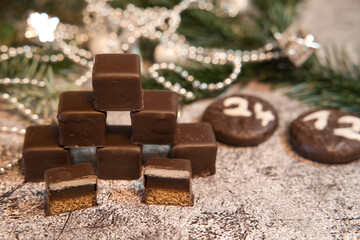 Stacked dominoes in front of fir trees and a Christmas chain with round chocolate cookies bearing...