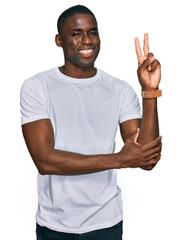 Young african american man wearing casual white t shirt smiling with happy face winking at the...