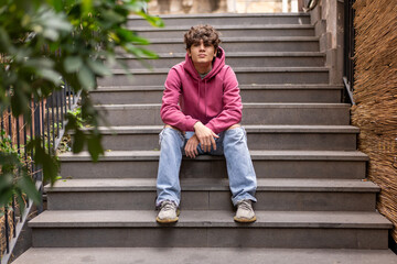 Relaxed teenager sitting on stairs outdoors, enjoying the urban environment in casual streetwear