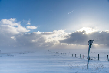 View over snowy agricultural landscape and snow covered road in Iceland with high winds creating...