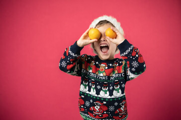 Merry Christmas. Funny child boy laughing and covering his eyes with tangerine. Happy New Year. Portrait of excited little kid wearing Christmas sweater having fun at home on Xmas night. Festive mood