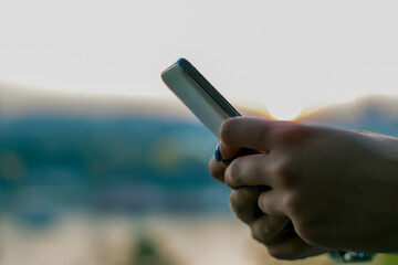 Close up view of female hands using smartphone near the river during sunset