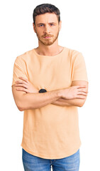 Handsome young man with bear wearing casual yellow tshirt skeptic and nervous, disapproving expression on face with crossed arms. negative person.