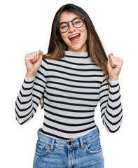 Young beautiful teen girl wearing casual clothes and glasses celebrating surprised and amazed for success with arms raised and open eyes. winner concept.