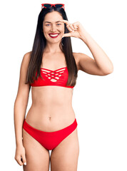 Young beautiful caucasian woman wearing bikini smiling and confident gesturing with hand doing small size sign with fingers looking and the camera. measure concept.