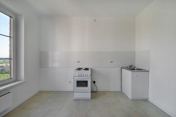 Kitchen with electric stove and sink after renovation. Kitchen in a new economy segment apartment without furniture